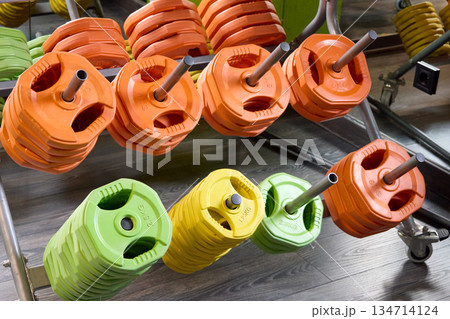Colorful weight plates organized on a rack in a gym, promoting fitness and strength training. 134714124
