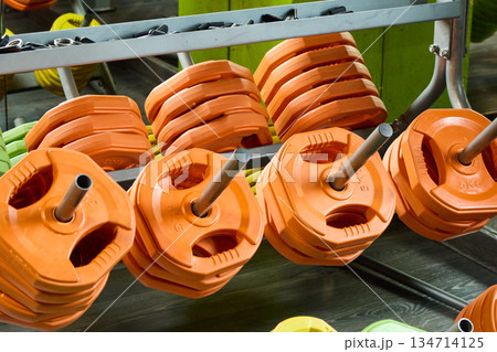 Orange weight plates stacked on a rack in a gym, showcasing fitness and strength training. 134714125