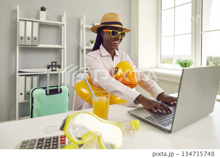 Funny woman sitting at the desk on workplace at office and booking tickets for summer vacation. Funny woman sitting at the desk on workplace at office and booking tickets for summer vacation. 134715748
