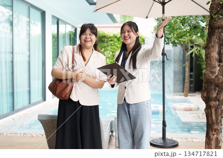 Real Estate Agents. Two women showcasing a property with a pool in a modern setting. Real Estate Agents. Two women showcasing a property with a pool in a modern setting. 134717821