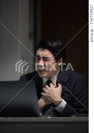 暗いオフィスで仕事が終わらず残業でパソコンの前でストレスで胸が痛いビジネスマン 暗いオフィスで仕事が終わらず残業でパソコンの前でストレスで胸が痛いビジネスマン 134718927