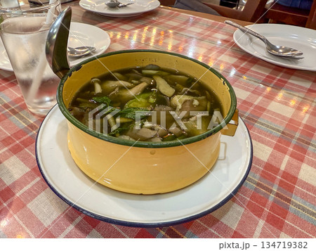 A clear herbal soup with vegetables and meat sits in a small enamel pot. The dish is served hot as a shared meal on a dining table. A clear herbal soup with vegetables and meat sits in a small enamel pot. The dish is served hot as a shared meal on a dining table. 134719382