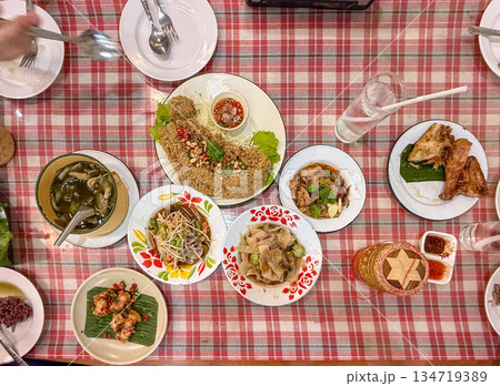 Topview of Isan food table with som tam, nam tok pork, grilled chicken, sticky rice basket. Local northeast Thai dishes arranged for casual eating. 134719389
