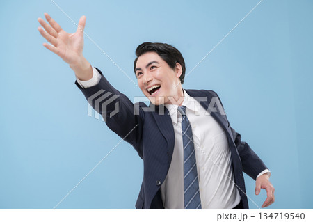 目標や未来を掴もうと手伸ばすスーツのジャンプや躍動感あるビジネスマン男性クローズアップ　水色背景 134719540