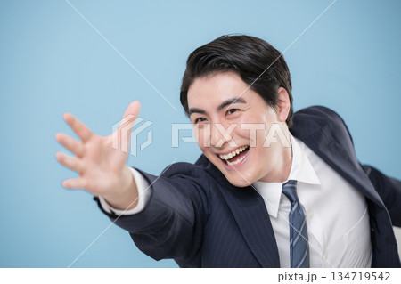 目標や未来を掴もうと手伸ばすスーツのジャンプや躍動感あるビジネスマン男性クローズアップ　水色背景 134719542