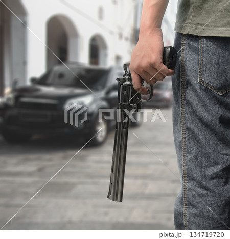 Man hand holding a revolver handgun in a blurred city street scene, suggesting crime, danger, and a tense situation. Concept of gun violence Man hand holding a revolver handgun in a blurred city street scene, suggesting crime, danger, and a tense situation. Concept of gun violence 134719720