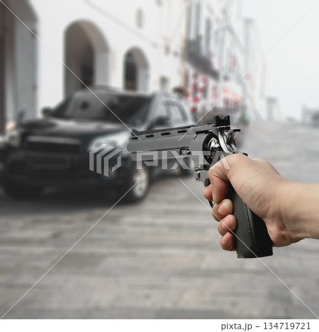 Man hand holding a revolver handgun in a blurred city street scene, suggesting crime, danger, and a tense situation. Concept of gun violence 134719721