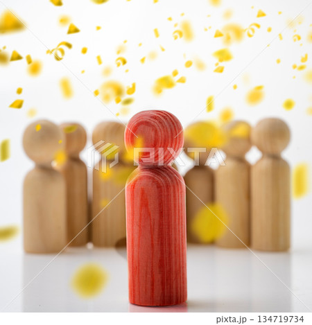 Wooden figure in red standing out from a crowd of beige figures, emphasized by falling yellow confetti. Concept of Winner Wooden figure in red standing out from a crowd of beige figures, emphasized by falling yellow confetti. Concept of Winner 134719734