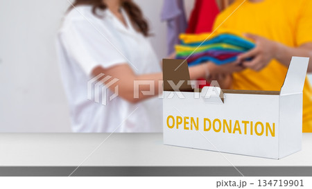 White box labeled "OPEN DONATION" sitting on a white table with people in the background donating colorful clothes. Charitable activities, volunteering, and donation drives White box labeled "OPEN DONATION" sitting on a white table with people in the background donating colorful clothes. Charitable activities, volunteering, and donation drives 134719901