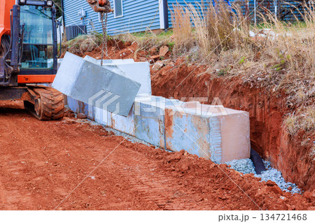 Heavy excavator is lifting placing cement blocks during construction work for retaining walls 134721468