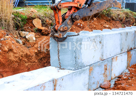 Excavator machine lifts concrete block as workers prepare for construction in building for retaining walls 134721470
