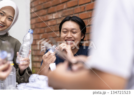Indonesian southeast asian people gathered outdoors, actively participating in recycling initiative. Decorating with plastic bottles promotes environmental sustainability. Spirit of eco-consciousness 134721523