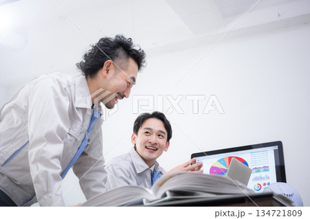 パソコンを見ながら笑顔でポシティブに話す作業着のビジネスマン2人 製造業などのdxやit化のイメージ パソコンを見ながら笑顔でポシティブに話す作業着のビジネスマン2人 製造業などのdxやit化のイメージ 134721809