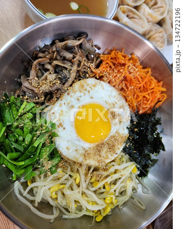 Bibimbap, a vibrant Korean rice dish topped with a variety of seasoned vegetables, gochujang, and a fried egg, often accompanied by sliced meat. Mixed together, it creates a flavorful and balanced. 134722196