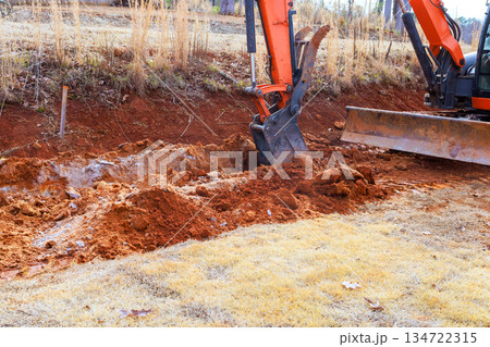 An excavator works to dig trench in earth at construction site An excavator works to dig trench in earth at construction site 134722315