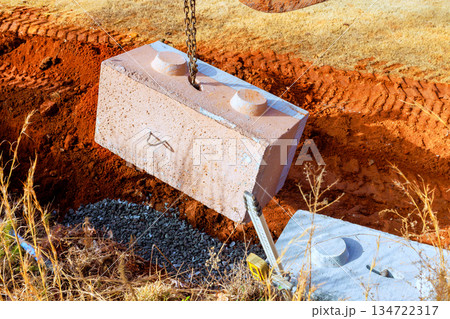 Large concrete block is being lowered with crane into hole at construction site 134722317