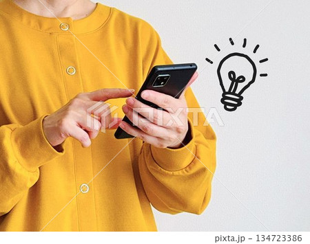 スマホを操作する女性と豆電球 スマホを操作する女性と豆電球 134723386