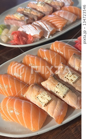 Fresh salmon sushi with bright orange slices placed on top of perfectly shaped rice, garnished with green leaves and radish for a simple, colorful, and appetizing presentation 134723546