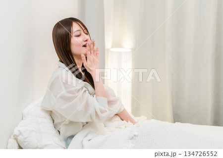 ベッドに起き上がりあくびをする若いアジア人女性 134726552