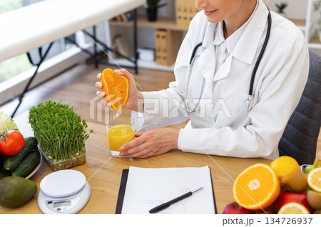 A doctor in a white coat squeezes fresh orange juice into a glass, surrounded by healthy food options. 134726937
