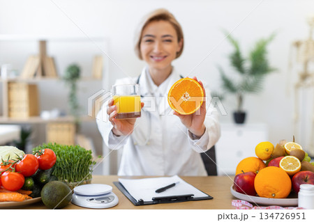 A nutritionist holds up a glass of juice and a sliced orange, promoting healthy eating and nutrition. A nutritionist holds up a glass of juice and a sliced orange, promoting healthy eating and nutrition. 134726951