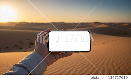 Mockup image of a hand holding mobile phone with blank screen in the middle of the desert 134727010