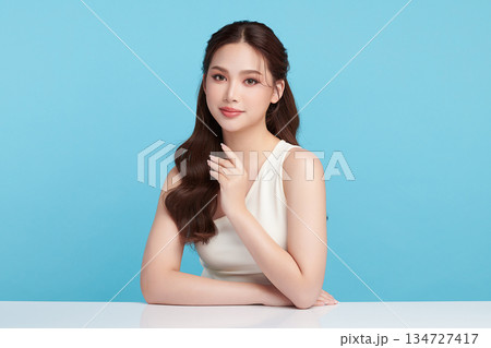 A beautiful young Asian woman with clean, fresh skin against a blue background. Skincare, facial treatment, cosmetology, beauty, and spa. An elegant portrait of an Asian woman. 134727417