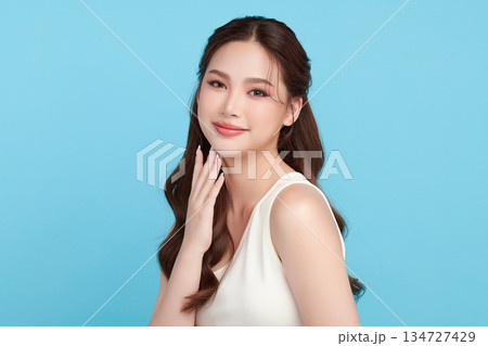 A beautiful young Asian woman with clean, fresh skin against a blue background. Skincare, facial treatment, cosmetology, beauty, and spa. An elegant portrait of an Asian woman. A beautiful young Asian woman with clean, fresh skin against a blue background. Skincare, facial treatment, cosmetology, beauty, and spa. An elegant portrait of an Asian woman. 134727429
