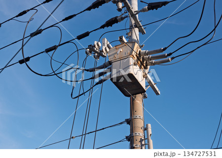 青空にそびえる電柱最上部の高圧柱上開閉器と配線、電力供給インフラの風景 134727531