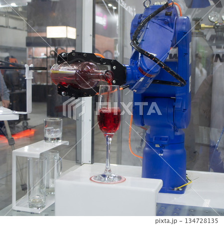 Robotic manipulators. Robot pouring liquid drink from bottle into glass. Industrial robot. Robot arm hand. Industrial manipulators for variety welding, material handling, palletizing. Robotization Robotic manipulators. Robot pouring liquid drink from bottle into glass. Industrial robot. Robot arm hand. Industrial manipulators for variety welding, material handling, palletizing. Robotization 134728135