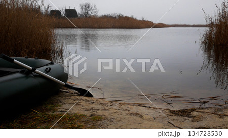 A rubber boat with an oar stands on the shore of a lake in autumn. A rubber boat with an oar stands on the shore of a lake in autumn. 134728530