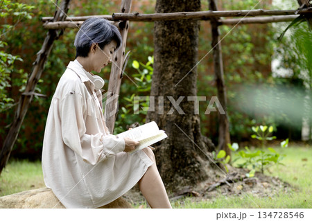 elderly woman sits on a rock reading a book in the garden enjoying elderly woman sits on a rock reading a book in the garden enjoying 134728546
