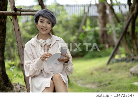 elderly woman sits on a rock reading a book in the garden enjoying elderly woman sits on a rock reading a book in the garden enjoying 134728547