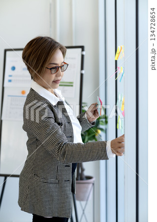 Senior business woman is looking at and writing messages on sticky notes Senior business woman is looking at and writing messages on sticky notes 134728654