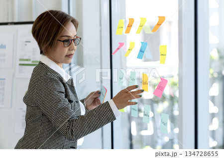 Senior business woman is looking at and writing messages on sticky notes 134728655