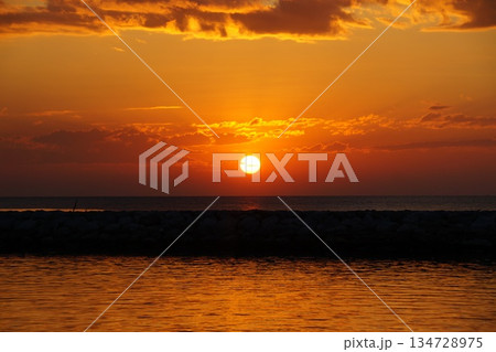 The red ball of a huge sun rises from the horizon. The sky is painted a bright orange. Summer, morning twilight.  134728975
