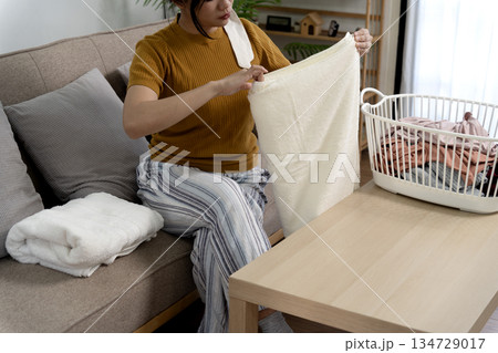 A young woman is sitting in the living room folding clothes modern woman A young woman is sitting in the living room folding clothes modern woman 134729017