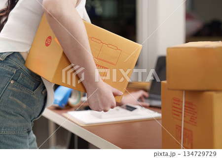 E-commerce. Woman carrying package while managing online business in home office. 134729729