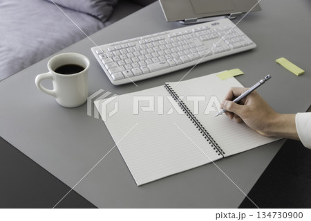 在宅ワークのデスク　ノートにメモを書く手元とコーヒー 134730900
