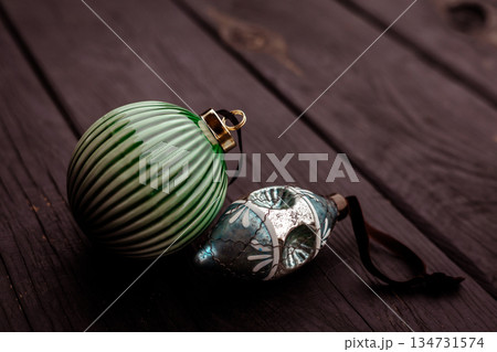 Two vintage New Year holiday ornaments lying on dark wooden surface. Elegant decoration in warm tones, cozy festive mood and rustic aesthetic Two vintage New Year holiday ornaments lying on dark wooden surface. Elegant decoration in warm tones, cozy festive mood and rustic aesthetic 134731574