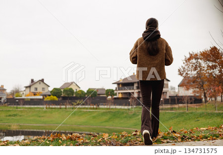 Stylish young woman walking outdoors in autumn park with smartphone, cozy brown outfit, calm mindful lifestyle, slow living female lifestyle. Stylish young woman walking outdoors in autumn park with smartphone, cozy brown outfit, calm mindful lifestyle, slow living female lifestyle. 134731575