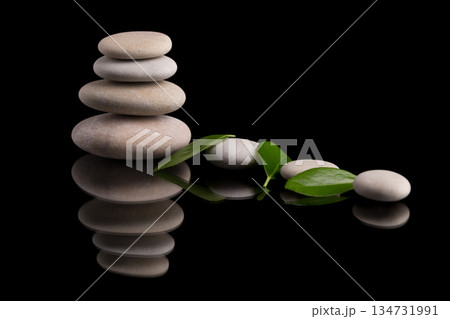 Zen stones stacked with fresh green leaves on black backdrop. Zen stones stacked with fresh green leaves on black backdrop. 134731991