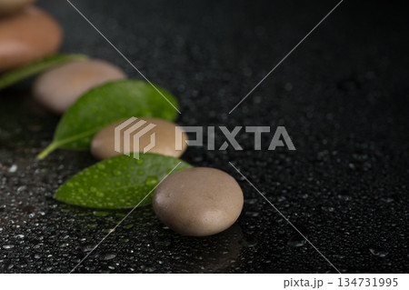 Smooth stones and green leaves with water droplets on black surface 134731995