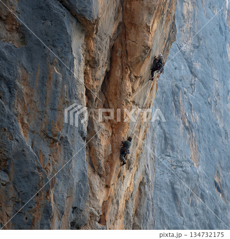 青空の下で険しい岩壁を登るロッククライマー 134732175