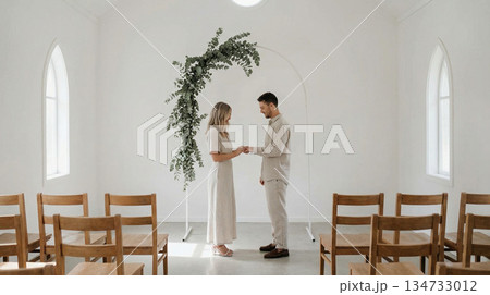白いチャペルでグリーンのアーチを背に指輪交換をするミニマルなウェディング 134733012
