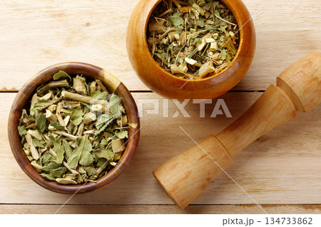Lemon balm, Melissa officinalis, dried leaves in two wooden bowls with a pestle on a rustic wooden table 134733862