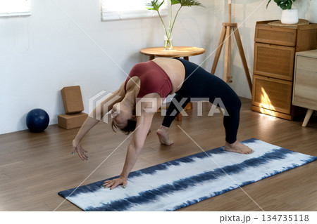 A fifty year old + woman doing yoga poses with her back stretched and her hands 134735118