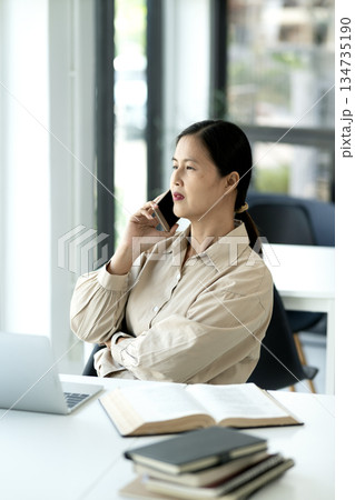 Elder female executive uses a mobile phone to talk at the desk 134735190