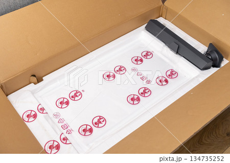 Open cardboard box containing new electronic device parts, featuring protective white foam and plastic bags with safety warnings, illustrating unboxing and product delivery 134735252