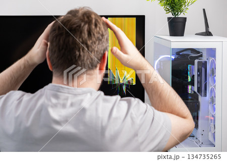 Upset man with hands on head seeing a broken computer monitor showing yellow lines, symbolizing a severe tech problem, hardware failure, and repair need Upset man with hands on head seeing a broken computer monitor showing yellow lines, symbolizing a severe tech problem, hardware failure, and repair need 134735265